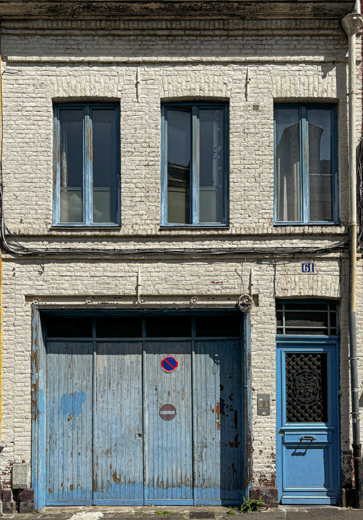 A small white brick house with blue shutters, whose charm still shines through despite the wear.